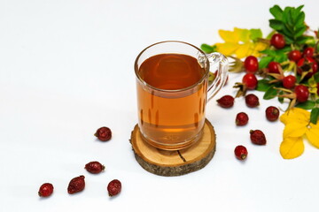 healthy rosehip tea in a glass Cup on a wooden saw, next to dry and fresh rosehip berries on a white surface
