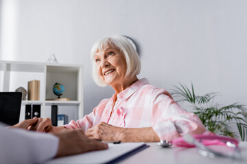 Selective focus of elderly woman holding hand with doctor while sitting at table