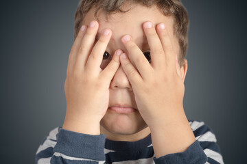 Childhood fear. A five-year-old boy covers his face with his hands.