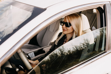 Fototapeta na wymiar Young blonde woman driving a car, smiling, wearing black sunglasses.