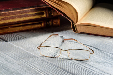 glasses lie on a wooden table next to old books.