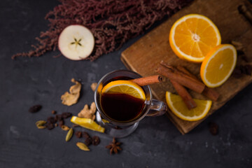 Obraz na płótnie Canvas Mulled wine in a glass for one, ingredients on a wooden board cinnamon sticks, raisins, anise, orange, apple on a gray background. New Year's homemade drink. View from above
