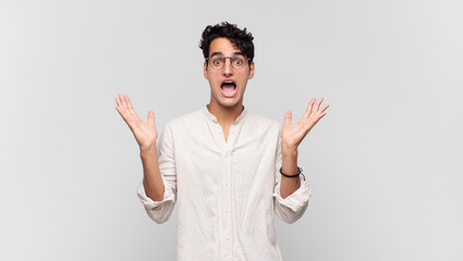 young handsome man feeling shocked and excited, laughing, amazed and happy because of an unexpected...