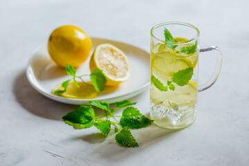 Lemon mint water, refreshing, morning drink, green mint leaves, yellow lemons on a white plate. light background