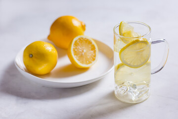 water with lemon in a transparent glass mug, three lemons on a white plate, lots of sunlight....