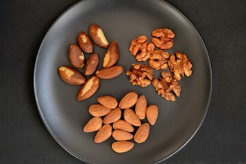 Almonds, brazil nuts and walnuts on a black plate on a black background close-up