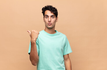young handsome man looking astonished in disbelief, pointing at object on the side and saying wow,...