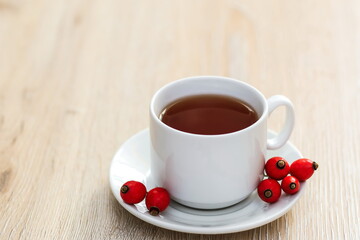 a white Cup of rosehip tea on a wooden surface, next to it are fresh rosehip berries, a place for text