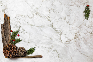 Christmas image/background.Pinophyta, brown pinecone with tree leaves, gift and red fruits on white marble.