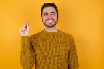 Young man wearing casual sweater and over isolated yellow background pointing up with hand showing up seven fingers gesture in Chinese sign language QÄ«.