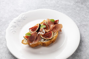 Croissant with figs, jamon, curd cheese and basil on a vintage plate