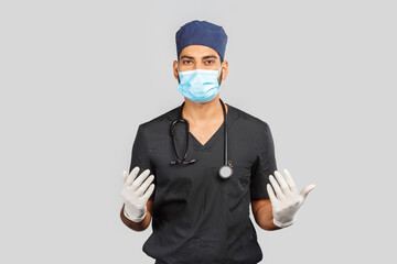 indian doctor or surgeon in black uniform with stethoscope and white latex gloves, blue medical mask on gray background