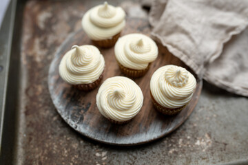 Mini muffins in paper cupcake holder on the wooden tray with white cream cheese frosting
