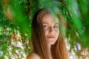 Young attractive woman standing under a yew green tree. He looks seductively at the camera