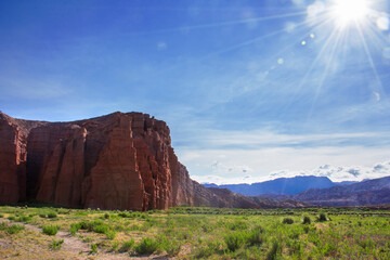 Montaña colorada con pradera verde  y cielo azul en día soleado