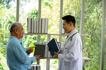 Asian medical doctor in hospital and old senior sick patient look for books on healthy living. Health care and medicine concept. new normal social distancing concept.