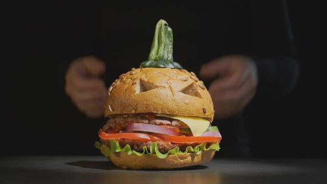 Female hands of waiter serve beef burger in image of pumpkin for Halloween on black background. halloween party dish.