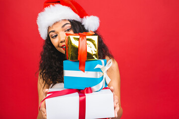 Beautiful smiling happy african american black woman in Santa Claus clothes isolated over red background. New year and christmas concept. Holding gift boxes.