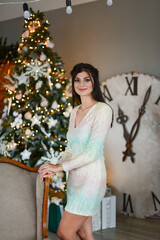 Fototapeta na wymiar The beautiful young lady standing in the Christmas room near Christmas tree and big clock