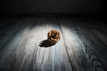 Abstract Christmas background with a pine cone highlighted by hard light surrounded by shadows on a natural wooden background. Side view, close-up. The concept of New Year and Christmas.