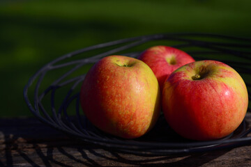 Three apples lie in a black fruit bowl made of a spiral made of iron in nature