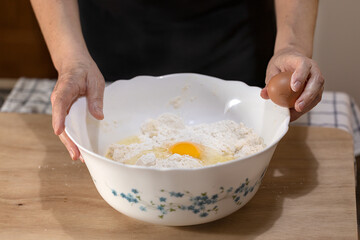 A bowl with flour and an egg and two female hands with an unopened egg.
