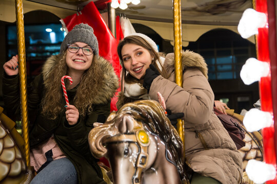 Two happy female friends riding on carousel