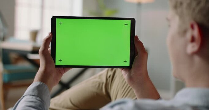 Close up shot of guy using a tablet computer with green mockup screen. Student during online lesson or work conference on self-isolation 4k footage