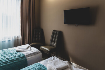 Bedroom interior design with tv on wall, chairs and beds with towels. Hotel or hostel room, motel or dorm look. Cozy guest house for travelers and tourists. Comfortable inn space to sleep over