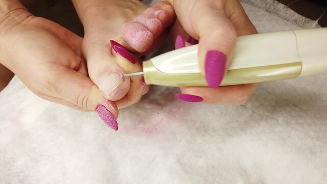 A girl at home does a pedicure, polishes her toenails with a special sanding machine, hardware manicure.