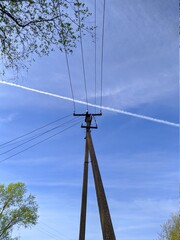 electronic pole with wires against the sky and a white plume from an airplane