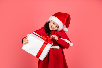 Merry Christmas and happy holidays. Winter holidays. Xmas gift shopping. Gift package. Cherished dreams. Boxing day. Small adorable girl Santa hat hold gift box. Kid hold present box red background