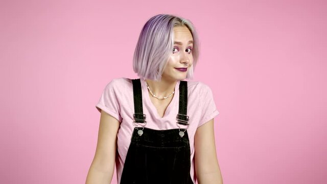 Young curly unsure girl with colorful hair shrugs her arms, makes gesture of I don't know, care, can't help anything .Young woman with trendy glitter freckles make-up