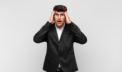 young handsome man feeling horrified and shocked, raising hands to head and panicking at a mistake