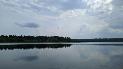 landscape of a blue lake and sky with white clouds on a forest background and also their reflection in the water during the daytime in summer