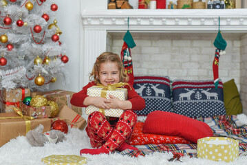Beautiful little girl holding a gift, in the bright New Year's interior