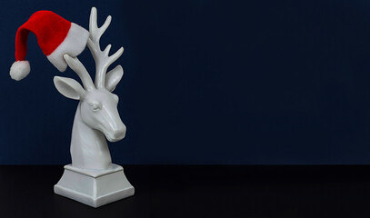 white deer in Santa hat on dark blue background, minimal creative concept of Christmas and New Year