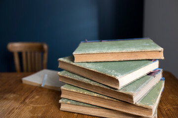 A stack of large, old, rag-bound books lie on a wooden table against a dark blue wall. Pen and notebook. Concept - back to school. Online training.