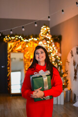 In Christmas room, surprised beautiful young girl keeping big green present in her hands.