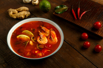 Tom yam soup with shrimp and lime in a light bowl next to lime, pepper chili and cherry.
