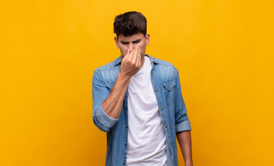 young handsome man feeling disgusted, holding nose to avoid smelling a foul and unpleasant stench
