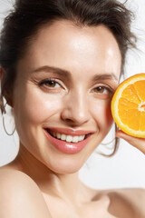 Close up portrait of young smiling female with perfect skin posing with slice of orange....