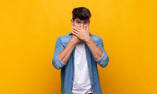 young handsome man covering mouth with hands with a shocked, surprised expression, keeping a secret or saying oops