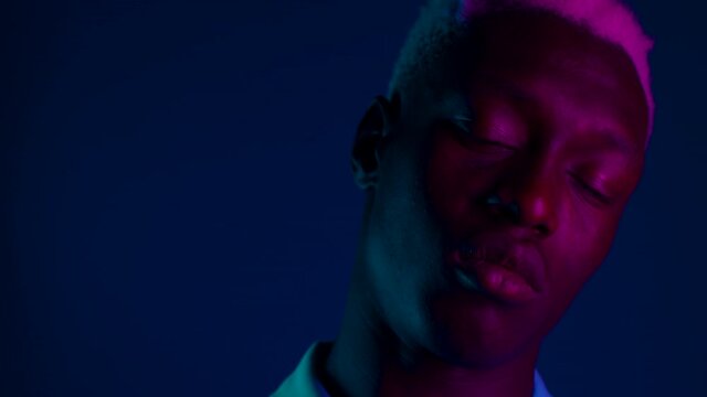 Young african american man moving head on dark blue background with pink neon light. Portrait of black guy with dyed white curly hairstyle.