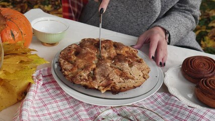 Woman cutting the pie. Autumn picnic near the pond in the autumn park. Cozy weekend picnic with red wine and food, candles and pumpkin, colorful fall leaves - Powered by Adobe