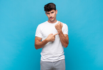 young handsome man looking impatient and angry, pointing at watch, asking for punctuality, wants to...