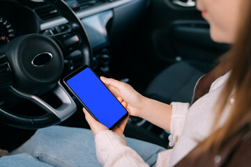 A young girl driver in a car. In the hands of a smartphone. Touchscreen. Template. Isolated smartphone with blue screen
