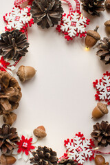 Fototapeta na wymiar Christmas frame of brown pine cones, acorns, red Christmas decorations and yellow lights, top view and white copy space