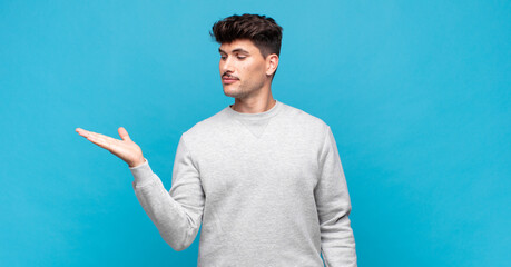young handsome man feeling happy and smiling casually, looking to an object or concept held on the...