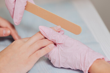 Manicure process. A master in pink rubber gloves processes the nails with a nail file. Female hands close up.